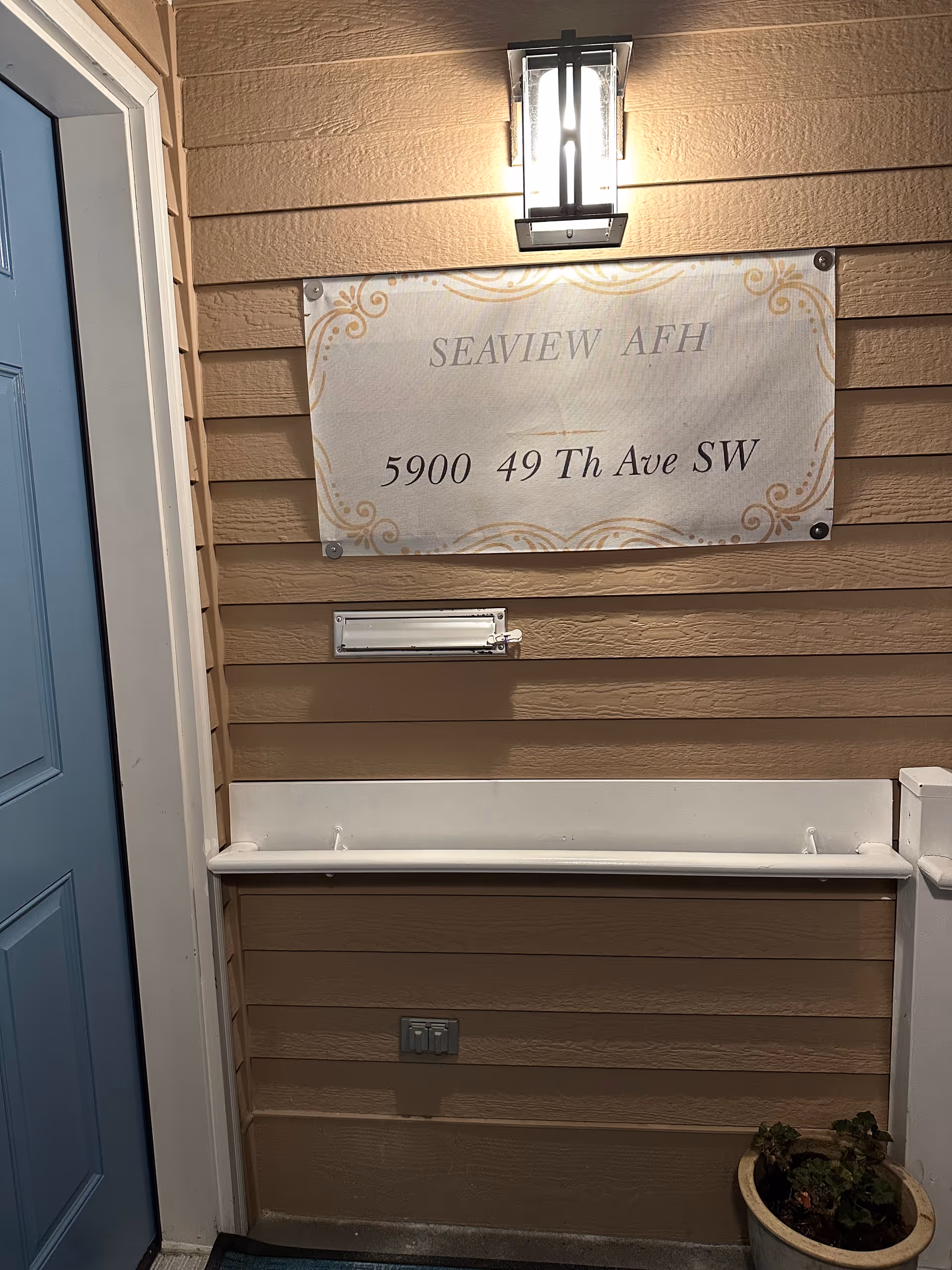 Exterior entrance of Seaview AFH with wall sign, light, blue door, and potted plant.
