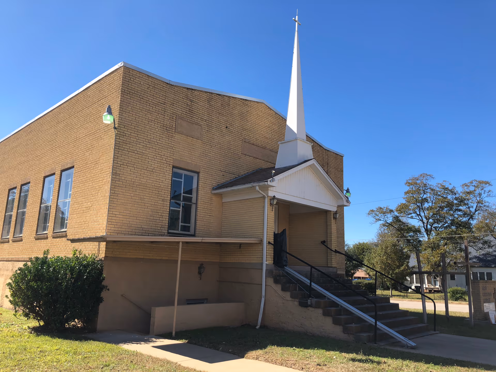 Brick building with a white steeple and front entrance, stairs and ramp under a blue sky.