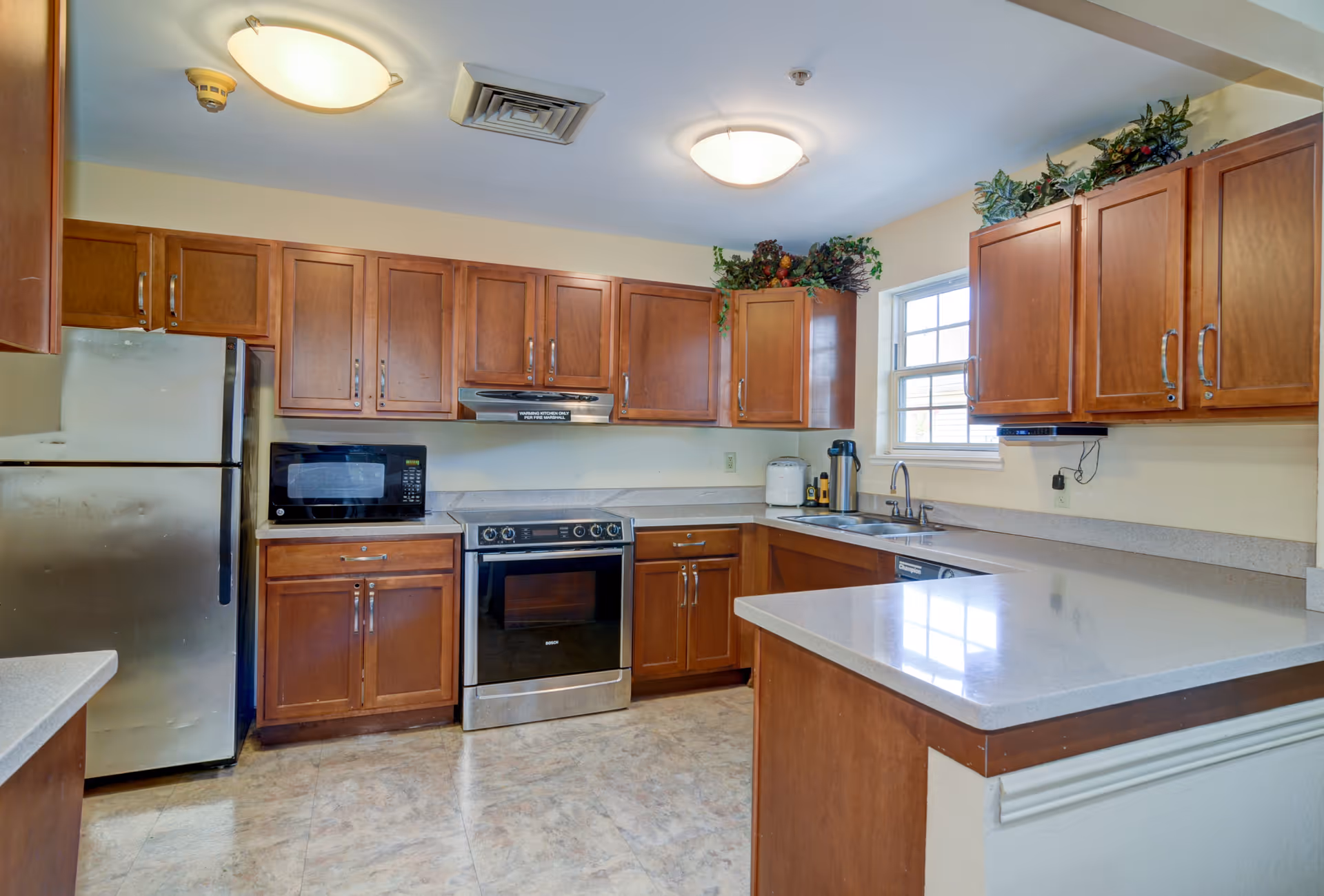 Senior living facility kitchen with wooden cabinets, stainless appliances, and a double sink.