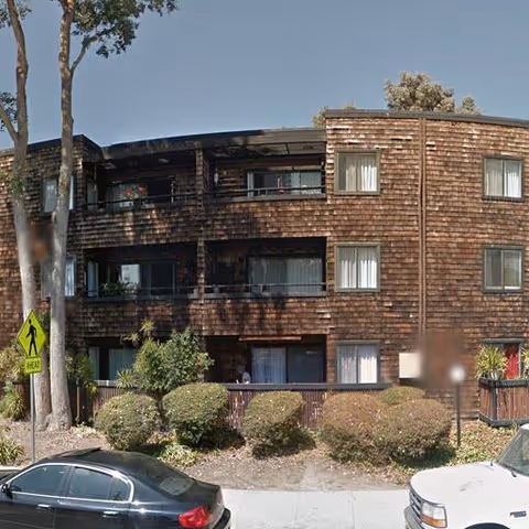 Exterior view of Redwood City Commons Apt: three-story wooden building with balconies and parked cars.