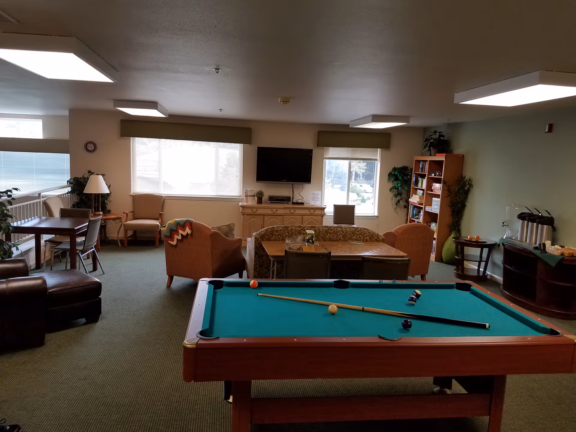 Interior senior living lounge with pool table, couches, TV, and bookshelf.