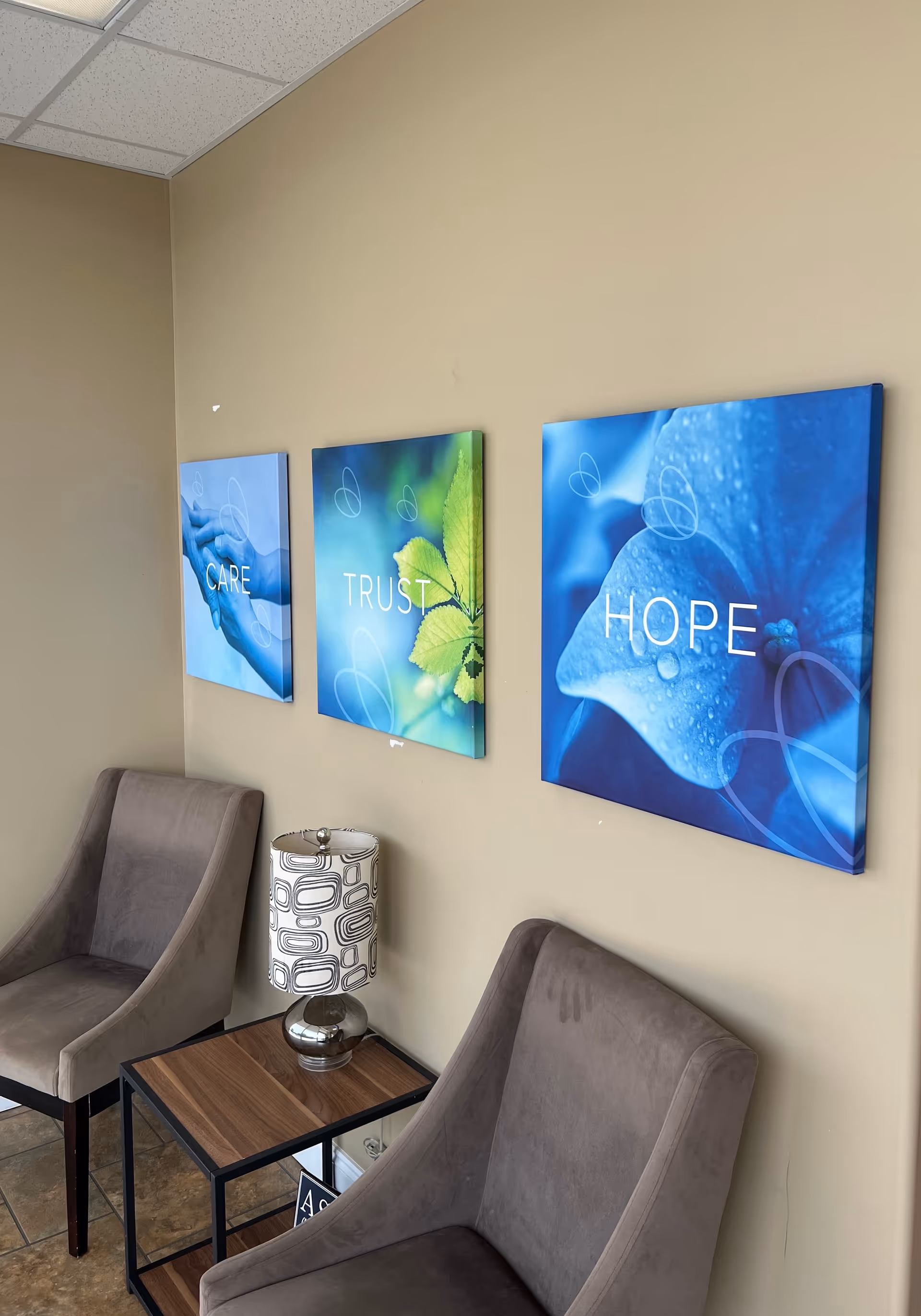 A waiting area with two gray chairs, a small table, and three blue wall art panels.