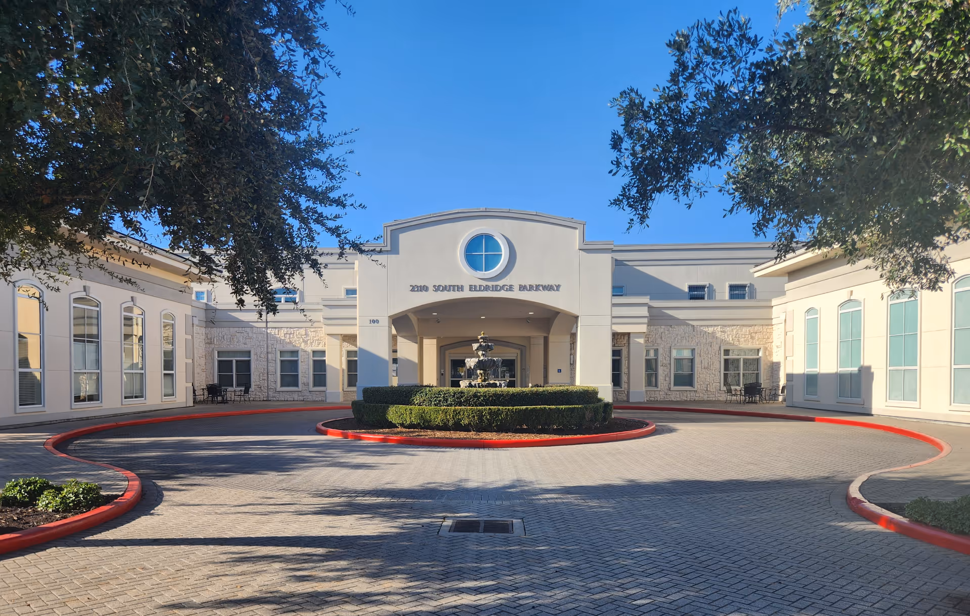 Exterior view of The Concierge senior living facility with circular driveway and fountain.