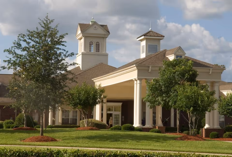 Front exterior of a senior living building with white columns, cupolas, and manicured landscaping.