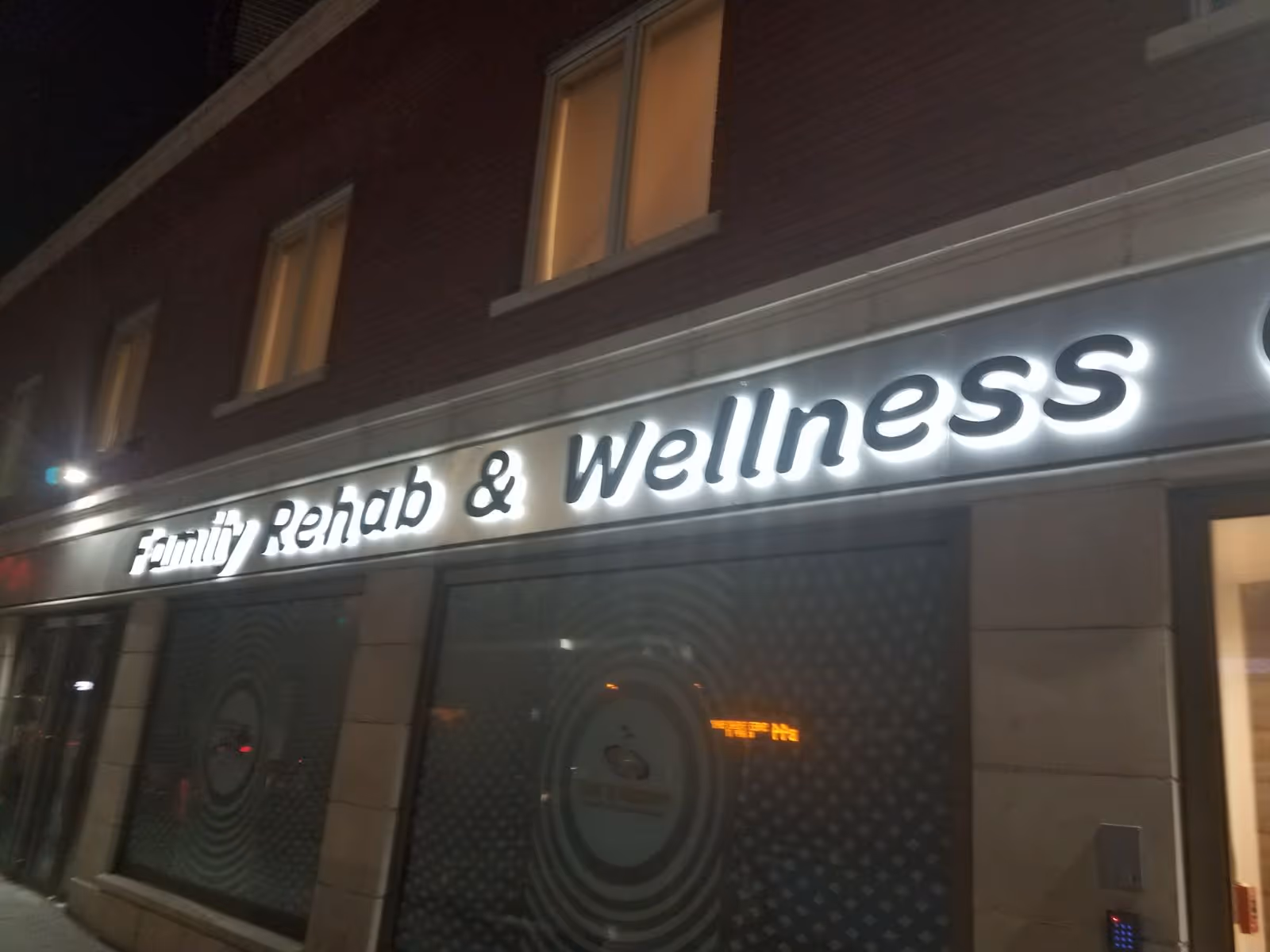 Nighttime exterior of a storefront with illuminated 'Family Rehab & Wellness' sign.