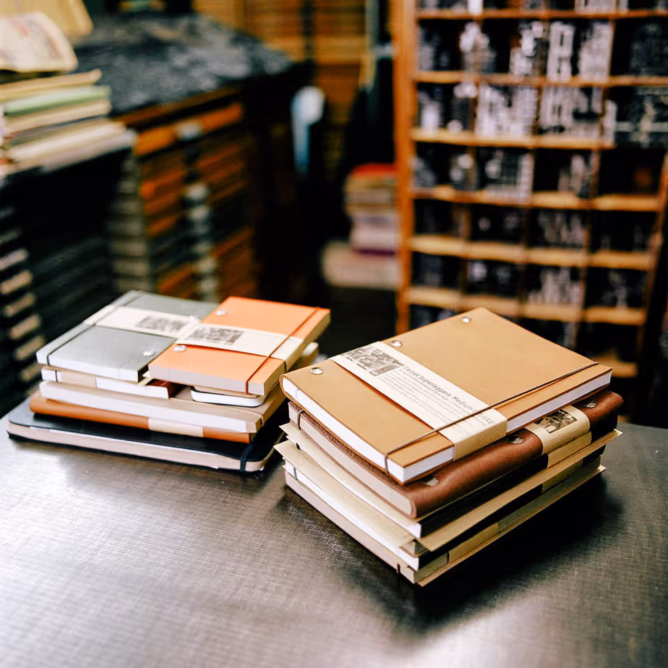 Stacks of bound notebooks on a metal table in a room with shelves.