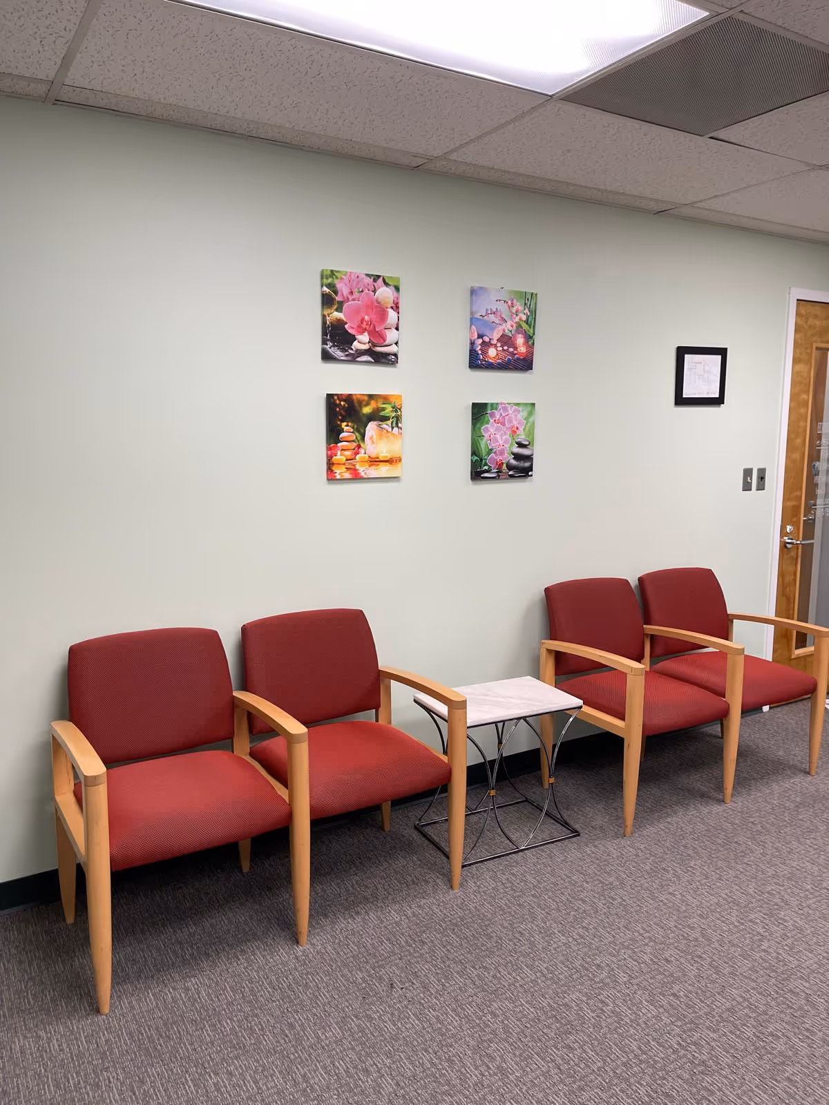 Waiting area with four red chairs, a small table, and wall art.