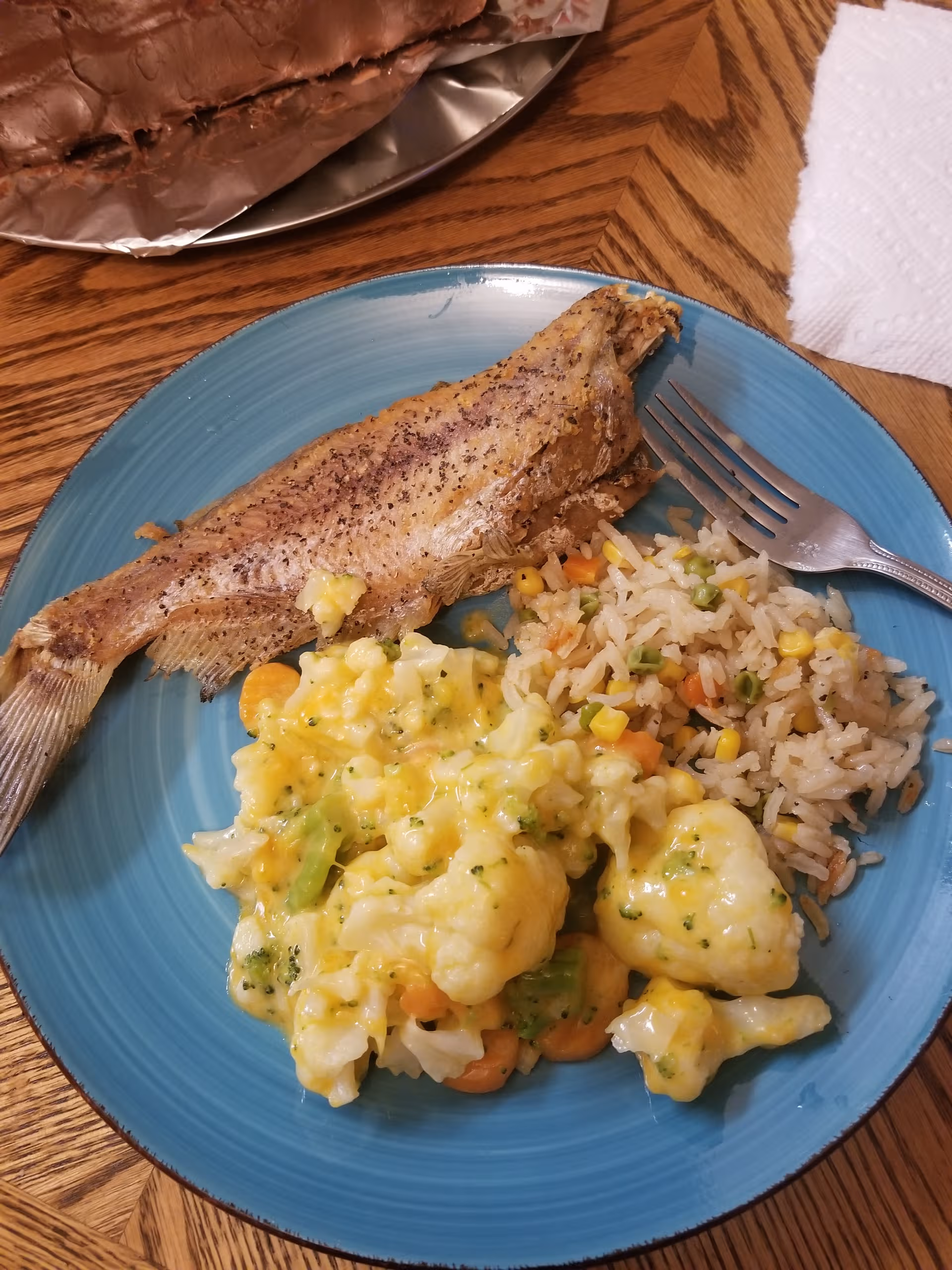 Whole fish with rice and creamy vegetables on a blue plate.
