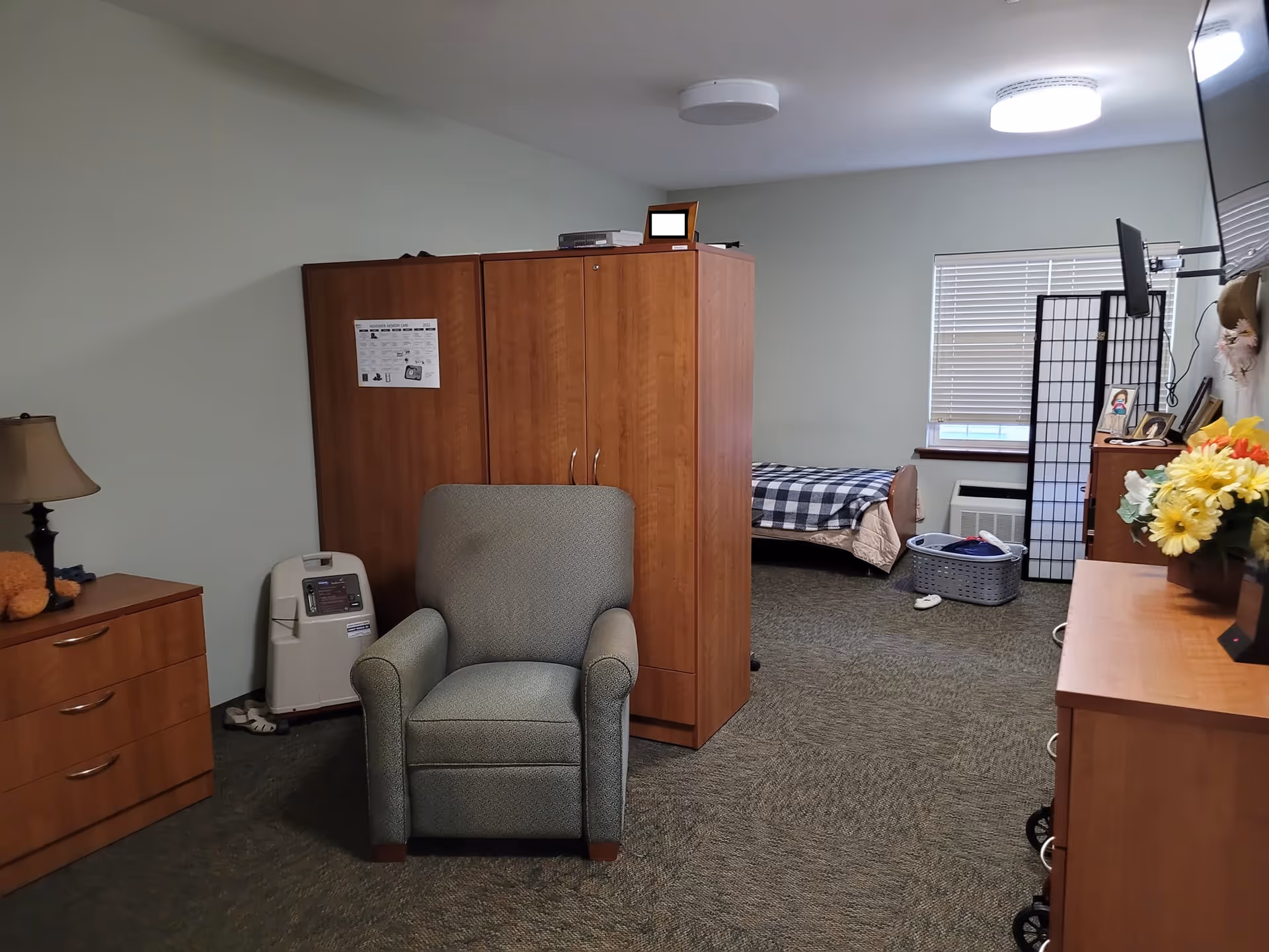 Senior living bedroom with bed, wardrobe, dresser, chair, and room divider.