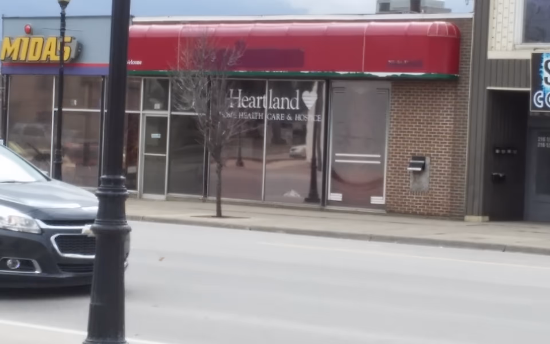 Streetfront view of Heartland Home Health Care storefront with red awning and glass windows.