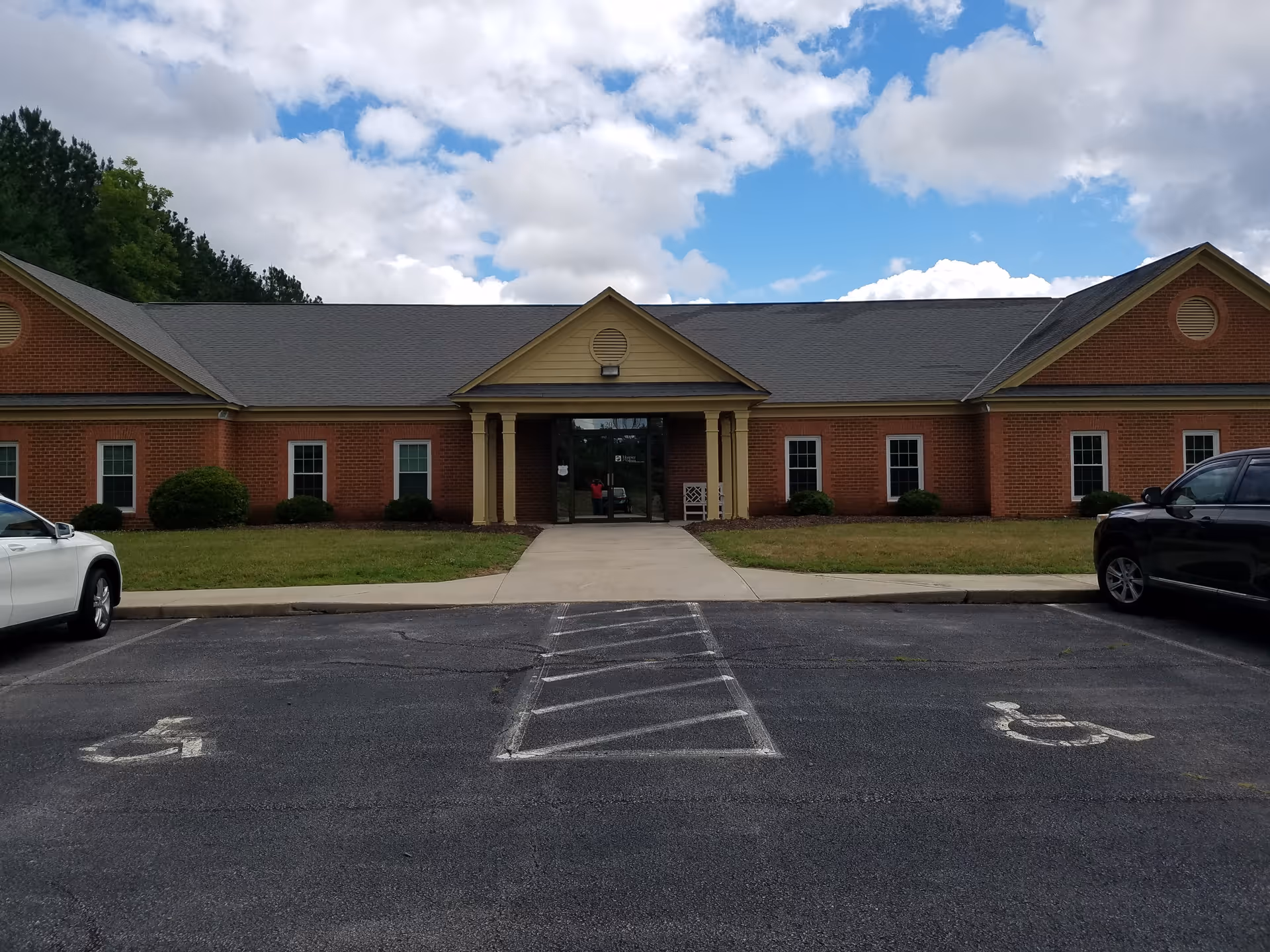 Exterior of a brick facility with central entrance and parking lot.