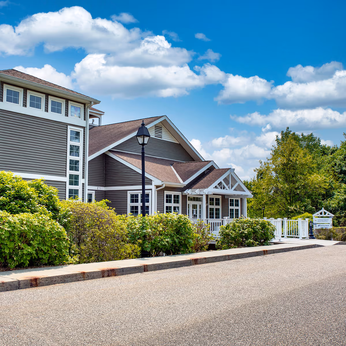 Exterior view of a gray, multi-gabled building with white trim and landscaped hedges.