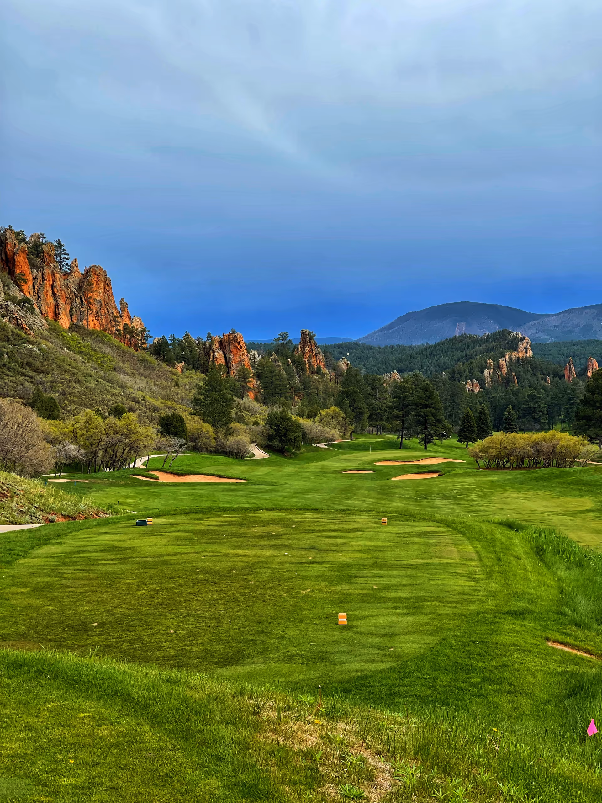 Broad view of a lush golf course with sand bunkers, trees, and distant rocky hills.