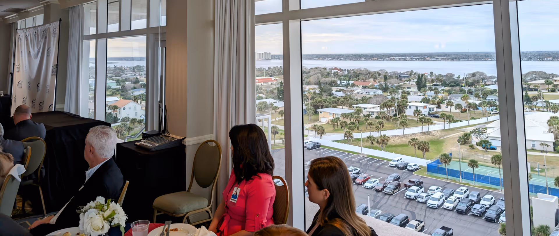 Residents sit at a round dining table in a room with large windows and a view.