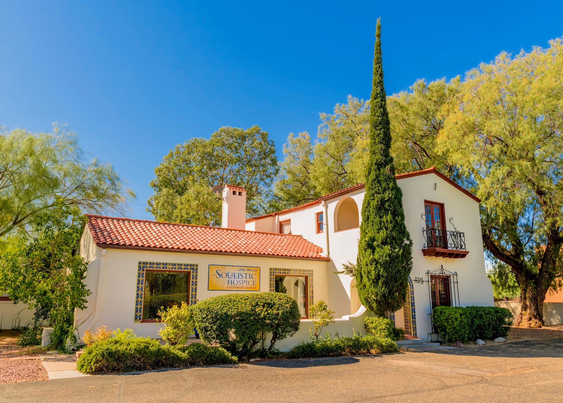 Soulistic Hospice exterior, white stucco building with a red tile roof and landscaped front yard.