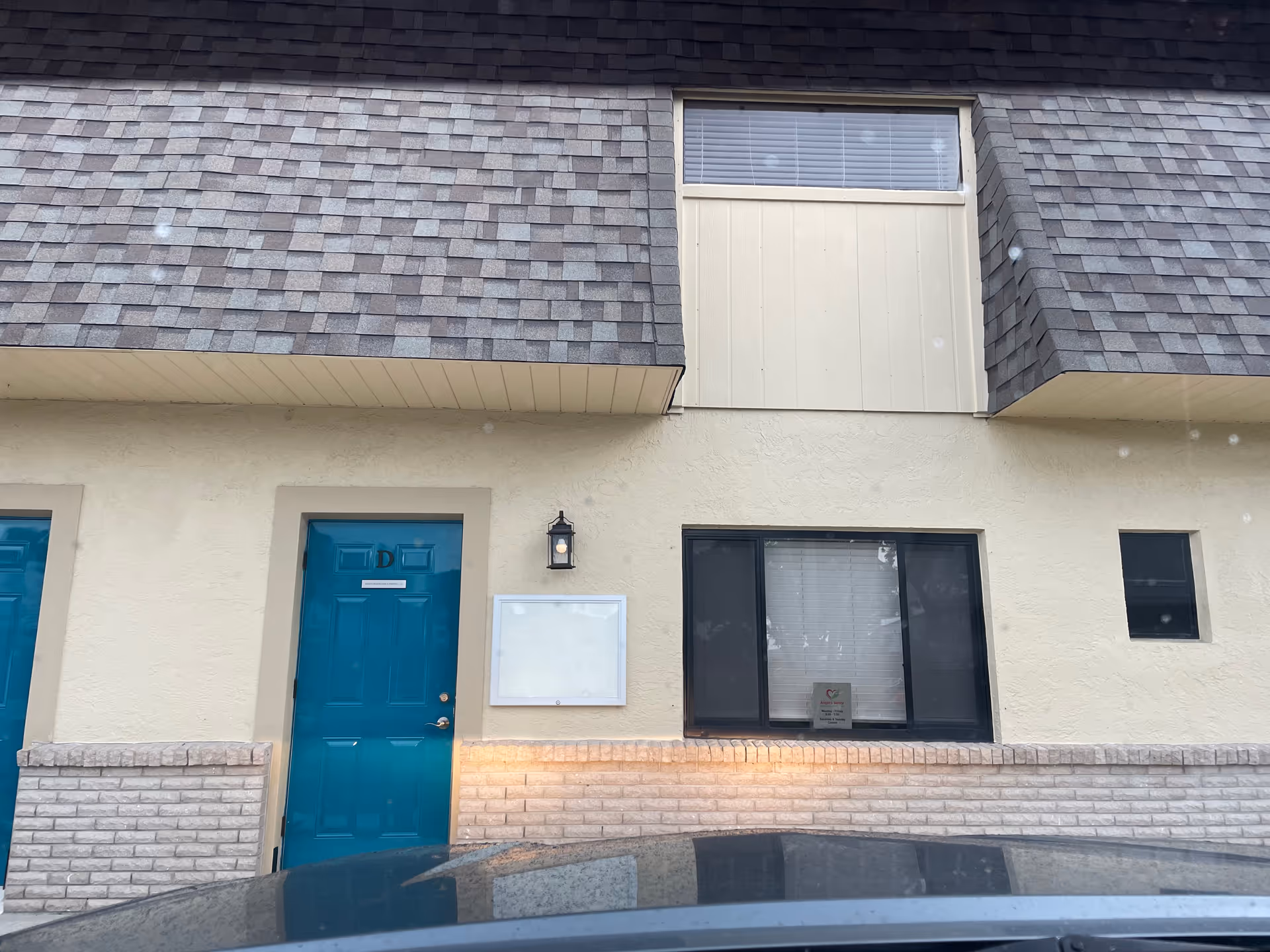 Exterior front of a beige stucco building with teal door and large window.