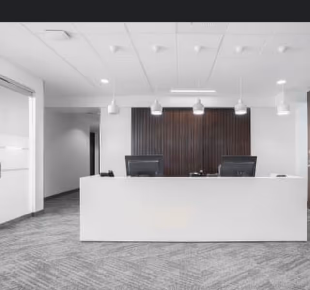 Bright modern facility reception with a white counter, dual computer monitors, and a dark wood backdrop.