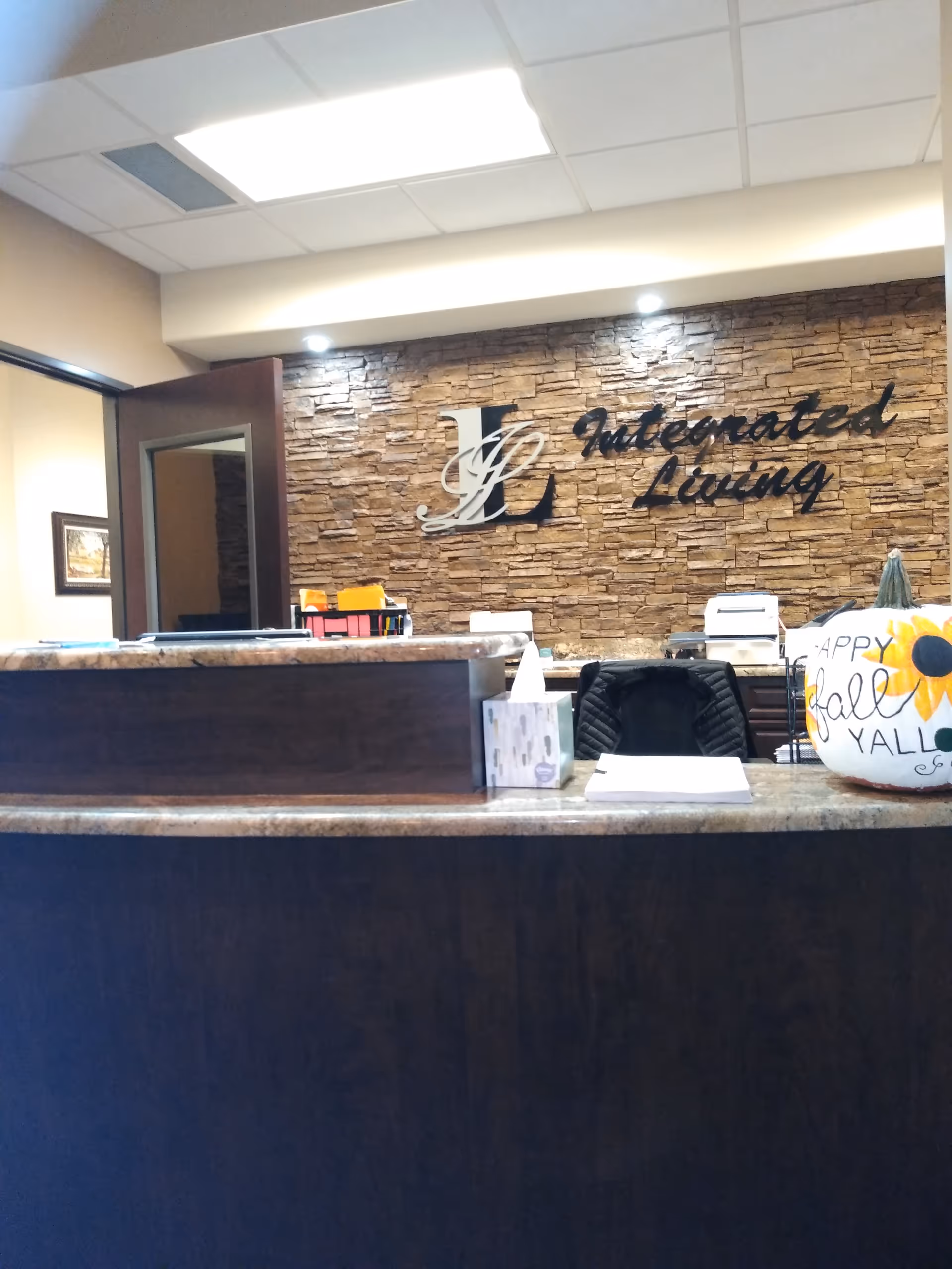 Front desk area with stone wall, logo reads Integrated Living, and office supplies.