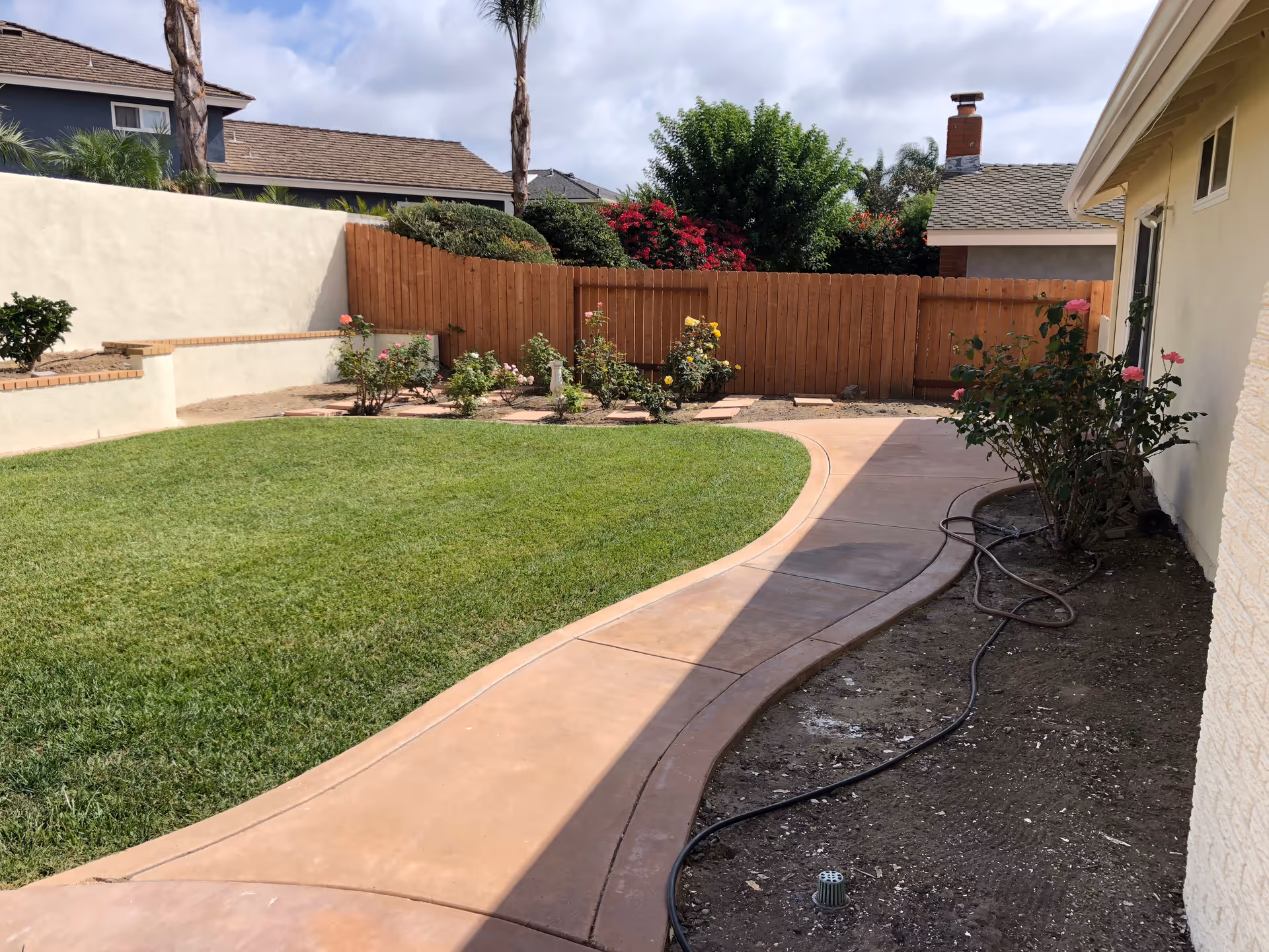 Curved walkway leads through a well-kept backyard with lawn, flowers, and fence.