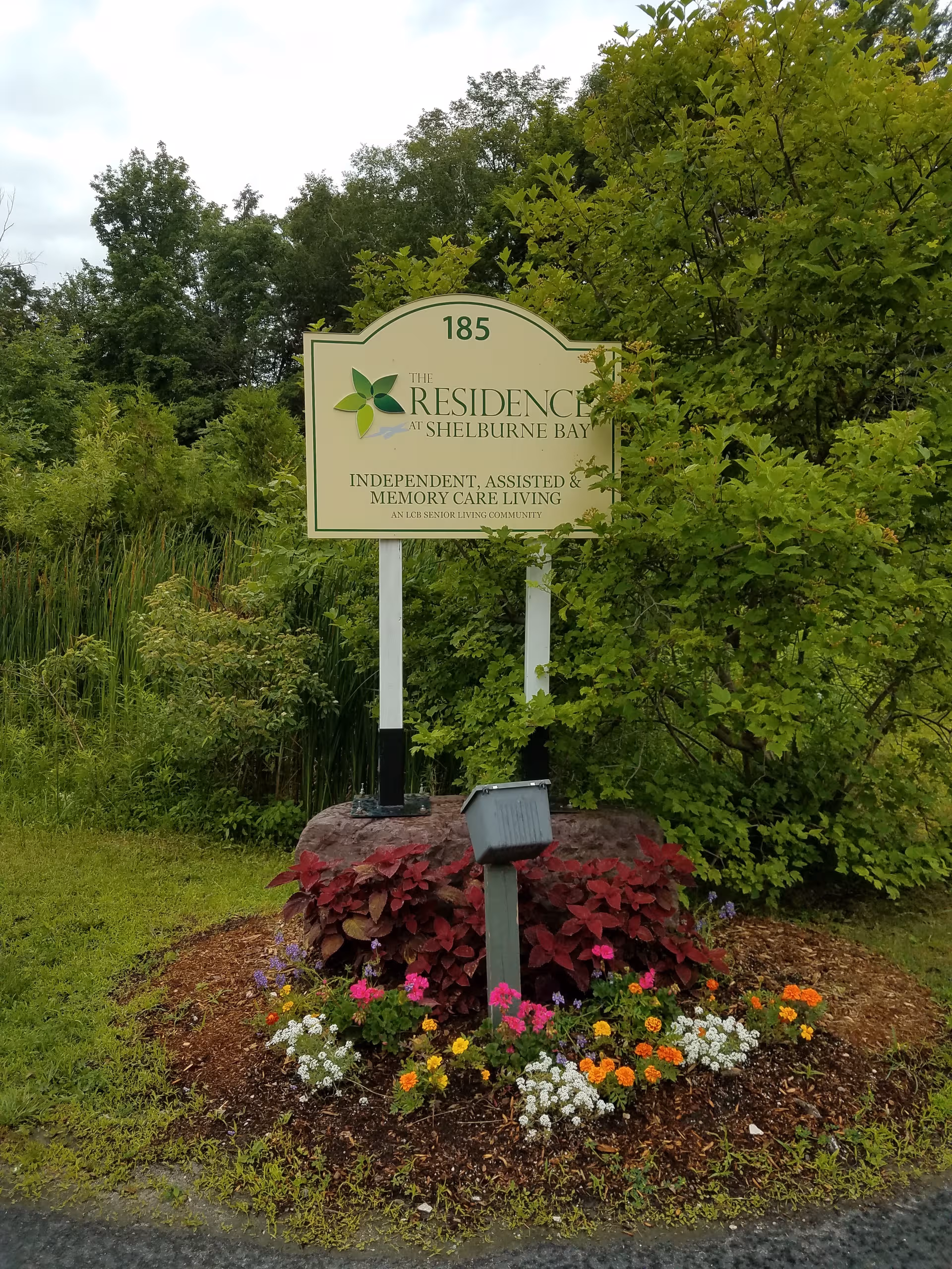 Outdoor garden sign for The Residence at Shelburne Bay with colorful flowers.