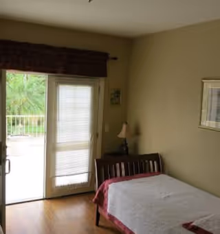 A bedroom with a wooden bed, nightstand, lamp, and sliding glass door to a balcony.