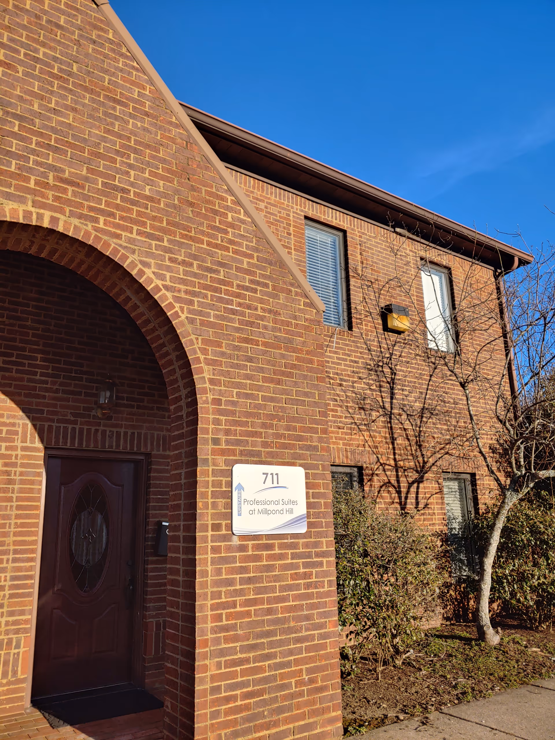 Brick building with arched front entry, doorway, and sign near windows under blue sky.