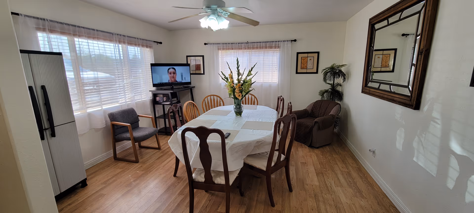 A dining room with a table, chairs, vase of flowers, and a TV in the corner.