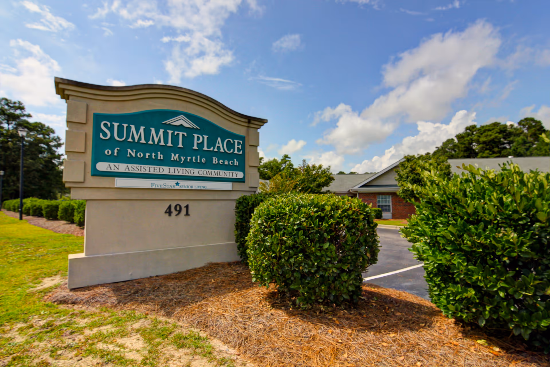 A large sign for Summit Place of North Myrtle Beach with shrubs and a driveway.