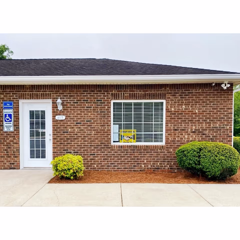 Brick exterior of a senior care facility with a white door, window, and shrubs.