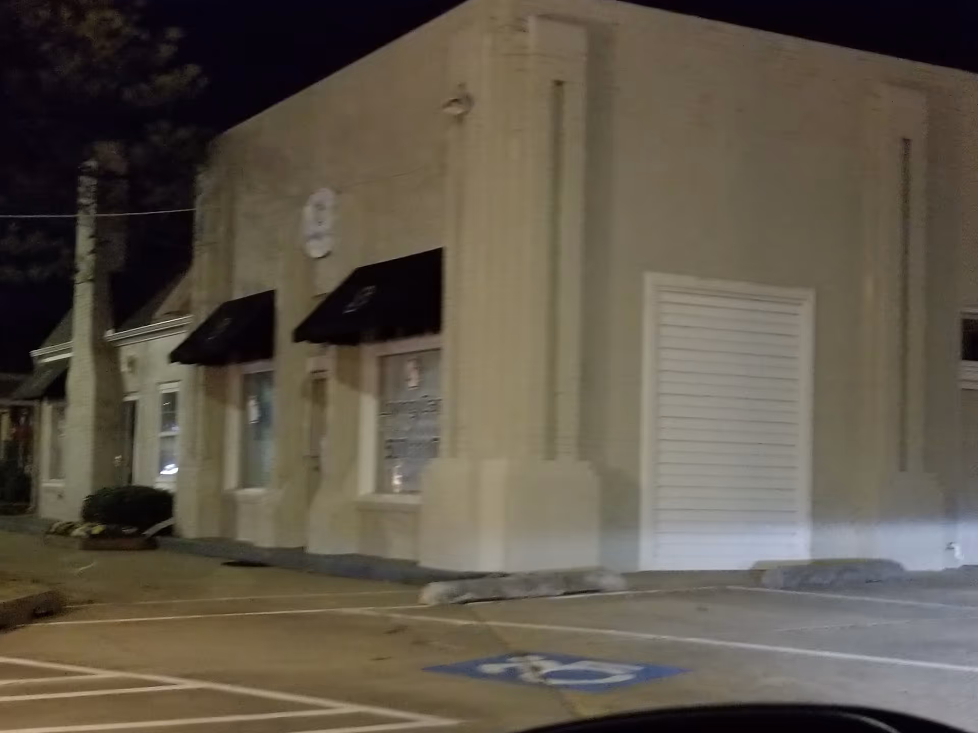 Night exterior view of a beige building with windows, awnings, and a white rolling door.