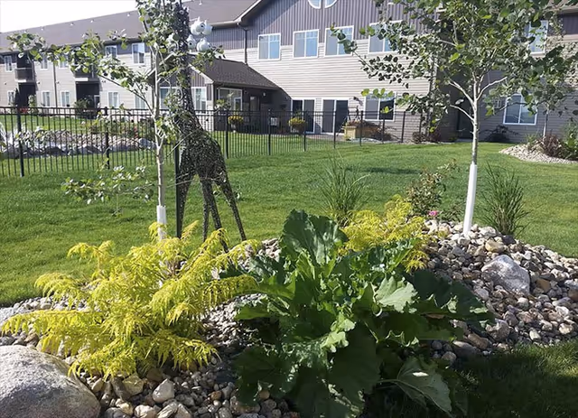 Lush landscaped outdoor area with rocks, plants, and a fence in front of Lakewood Landing.