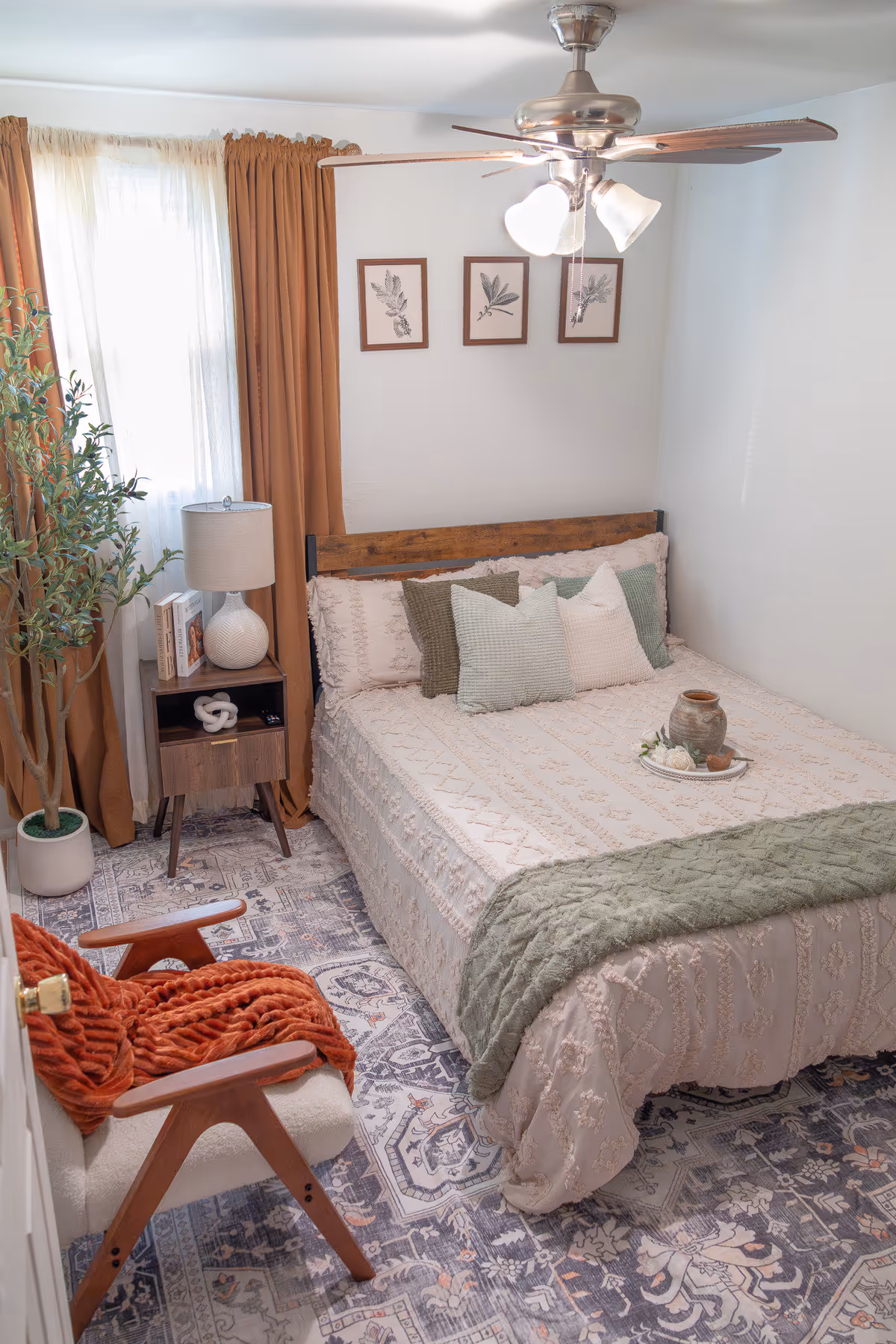 Cozy bedroom with bed, nightstand, plant, curtains, rug, and ceiling fan.