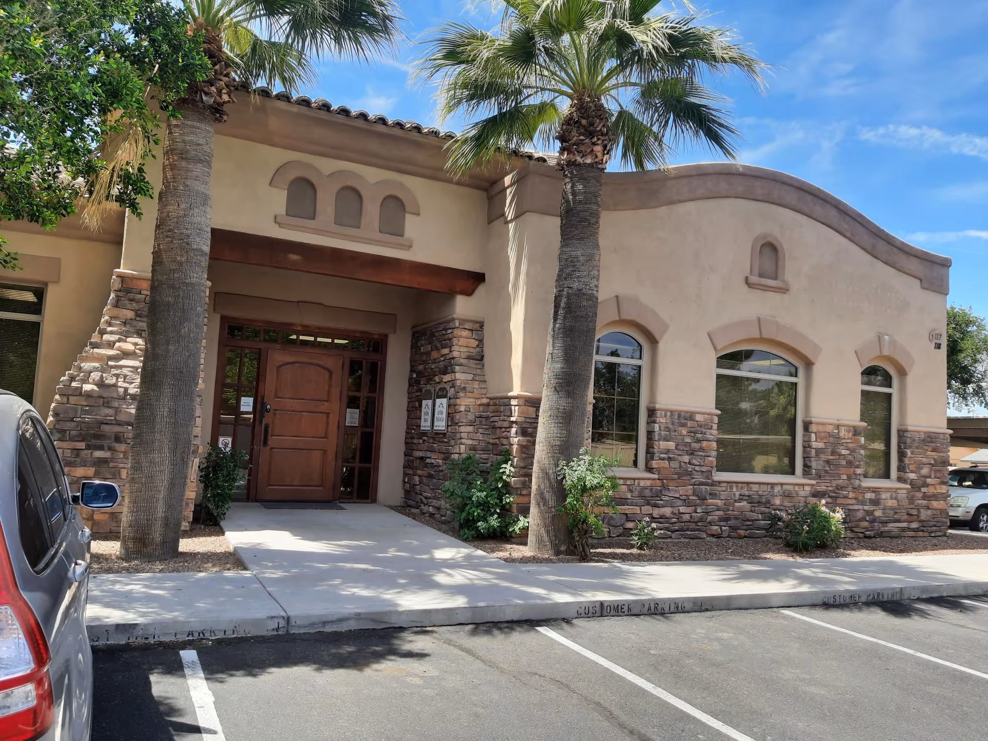 Exterior of a palliative care facility with a wooden entrance door and palm trees.