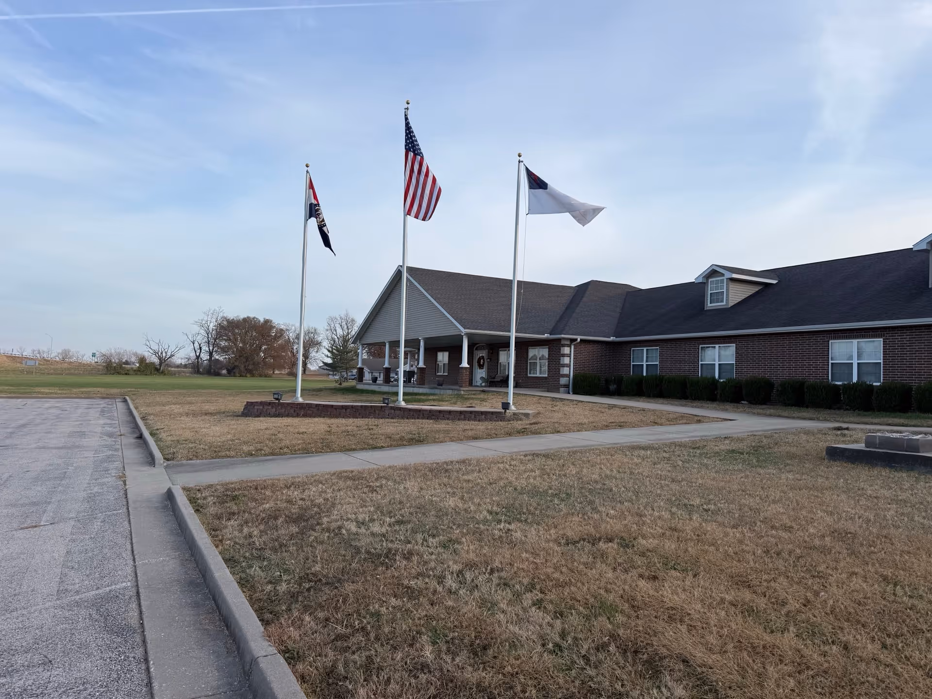 Exterior of a single-story brick senior care home with flagpoles and a front entrance.