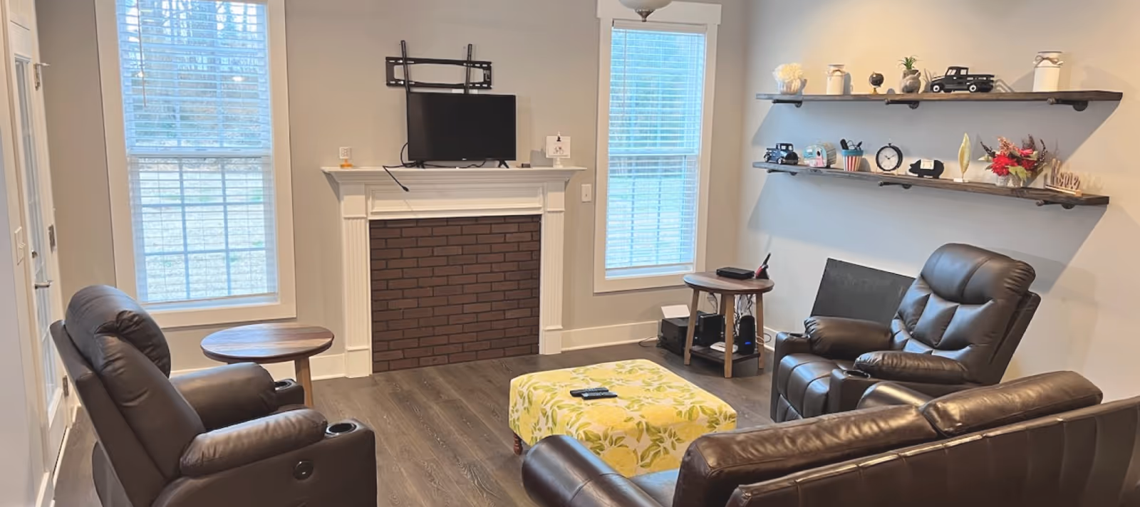 Cozy lounge area in a senior home with leather recliners, a brick fireplace, and wall shelves.