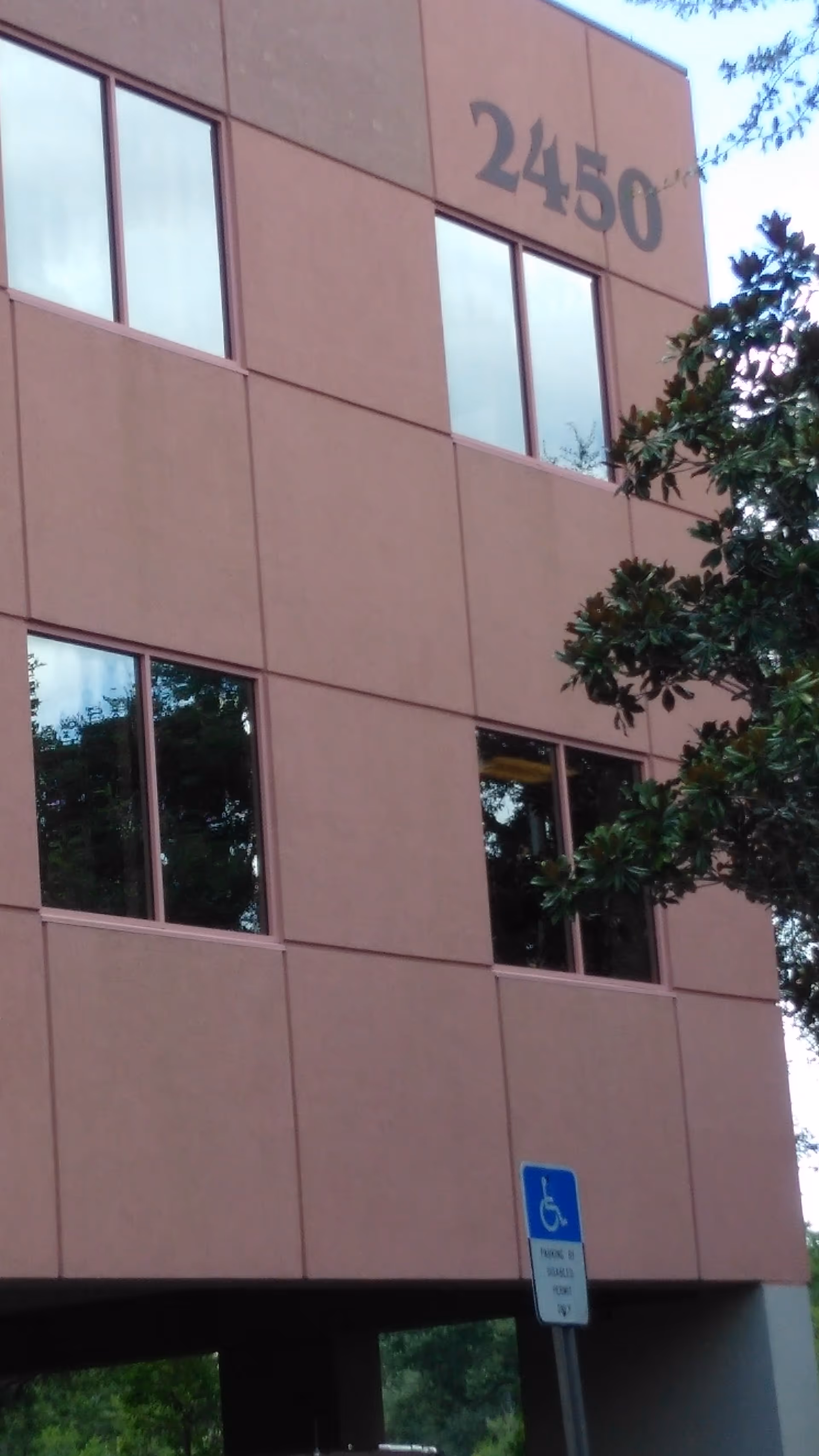 Exterior view of a beige building facade with large windows and a handicap sign.