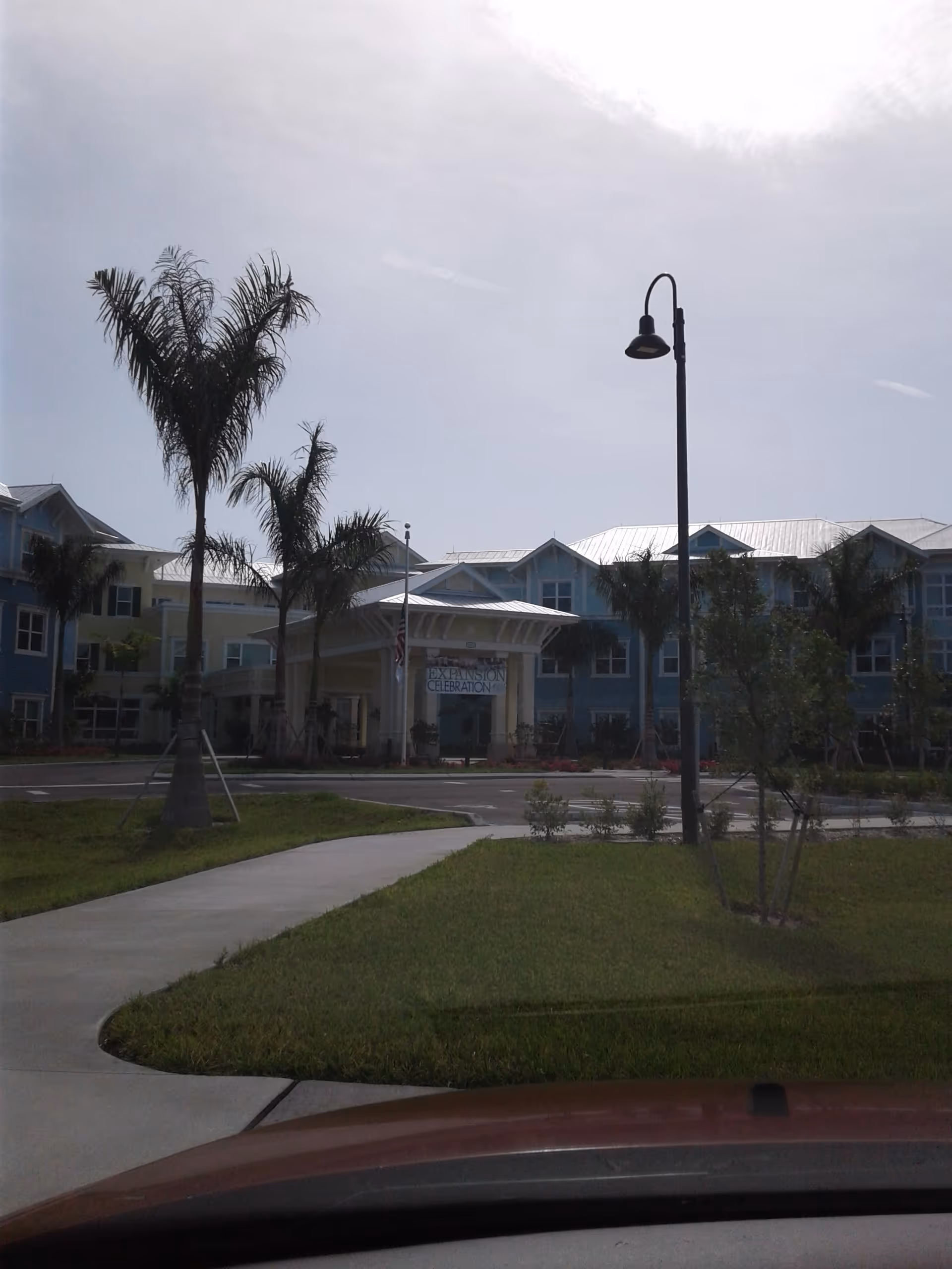 Exterior view of a Gulf Coast Village senior living building with palm trees and walkway.