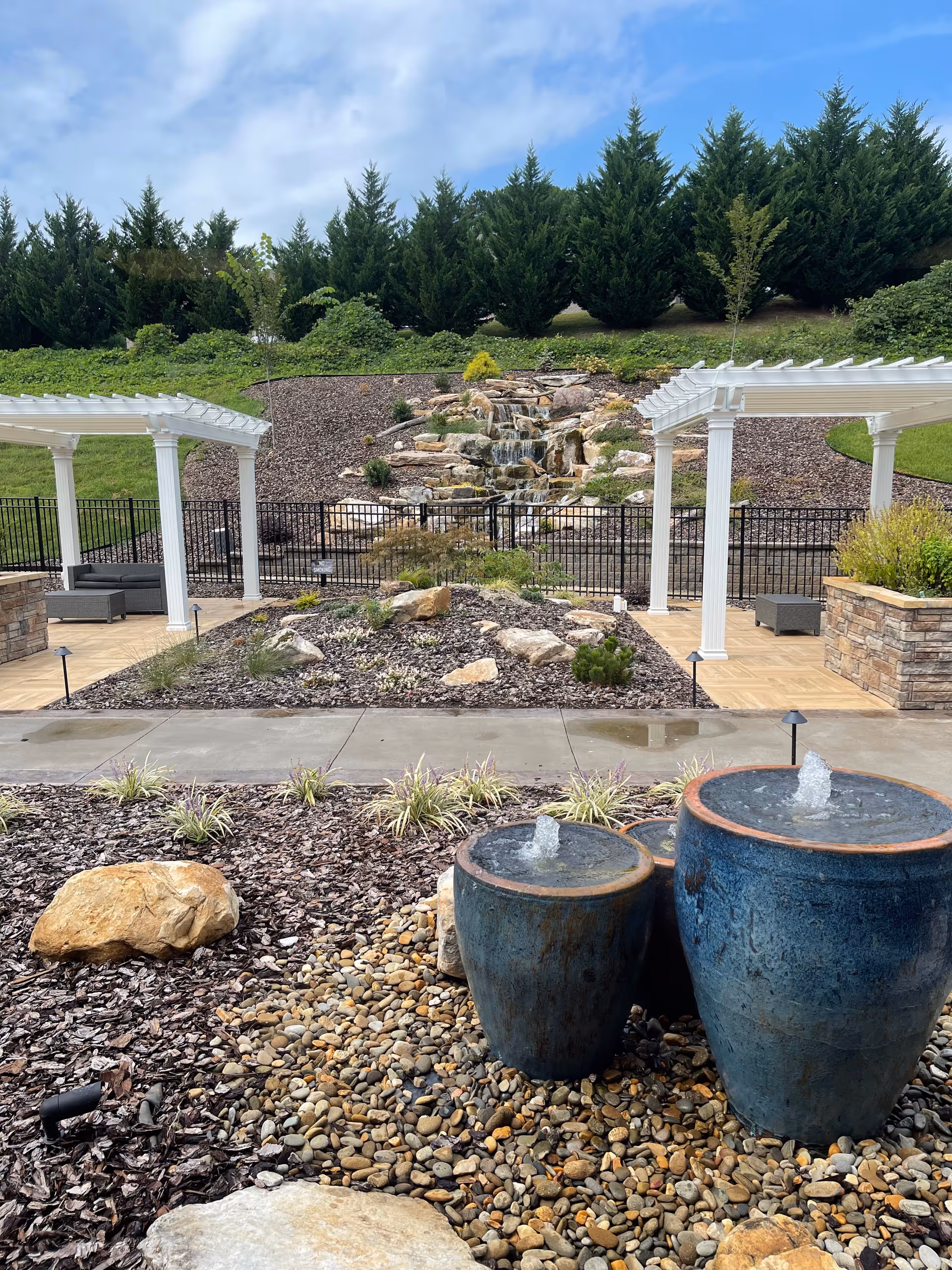 Outdoor landscaped courtyard with cascading waterfall, rocks, and blue fountain pots.