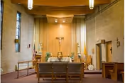 Interior chapel with altar, crucifix, pews, and flags in a nursing home facility.