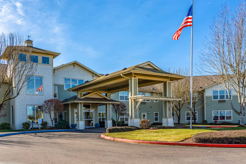 Front view of a senior living facility with entrance and flagpole on a sunny day.