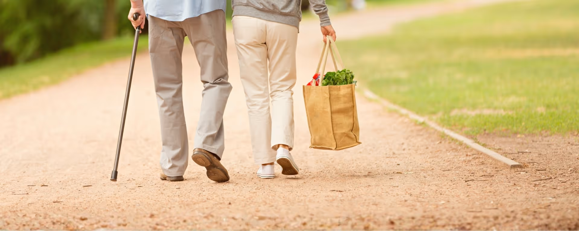 Two people walk along an outdoor path, carrying a grocery bag.