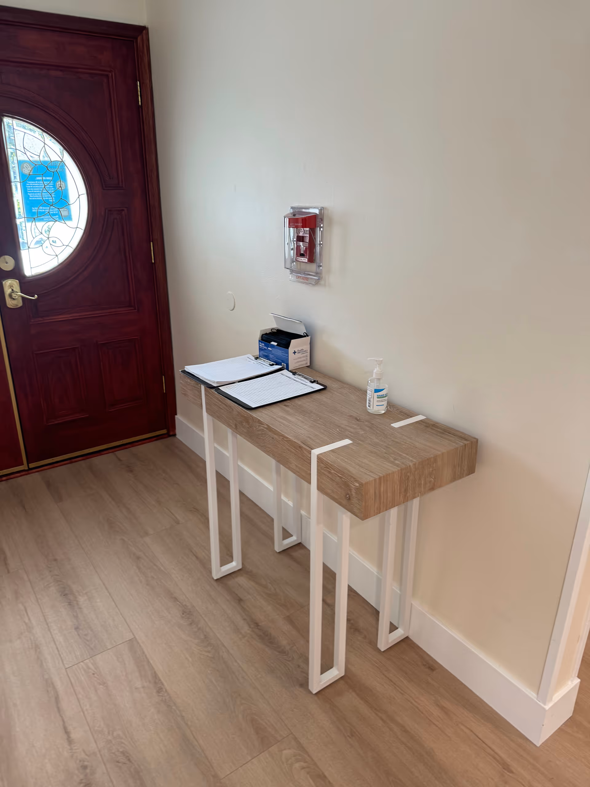 A wooden console table with sanitizer and papers beside a front entry door inside.