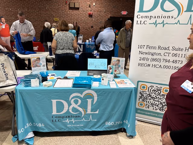Indoor expo booth for D&L Companions senior living with a blue table and visitors nearby.