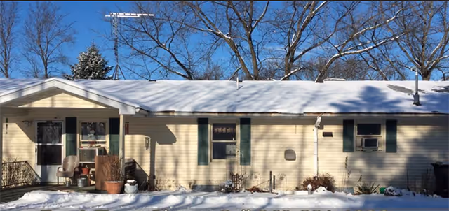 Single-story beige building with snow-covered roof and front entrance with chairs outside