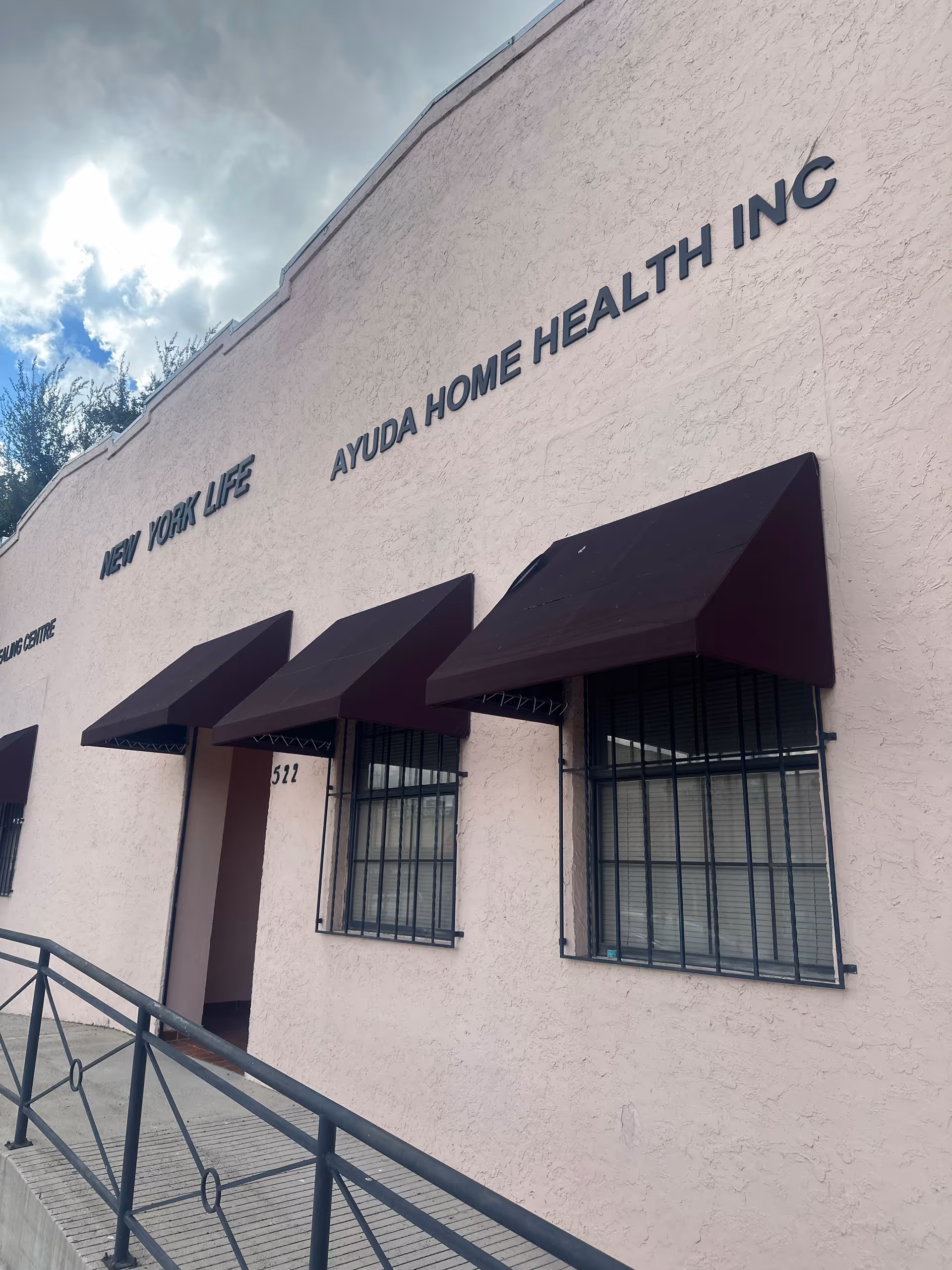 Exterior view of a pink building with Ayuda Home Health Inc signage and canopies.
