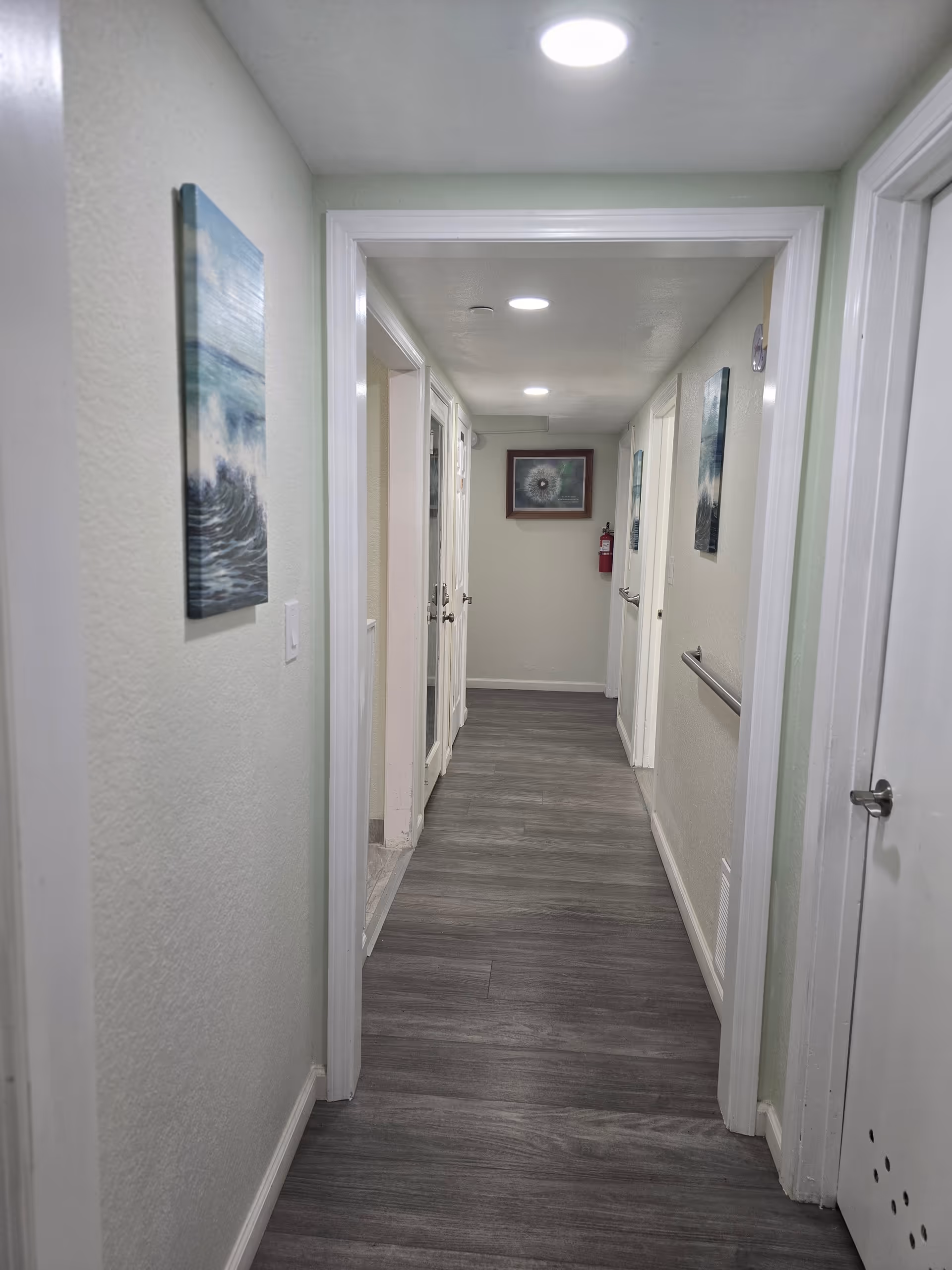 Interior hallway of a senior living facility with doors, artwork, and overhead lights.