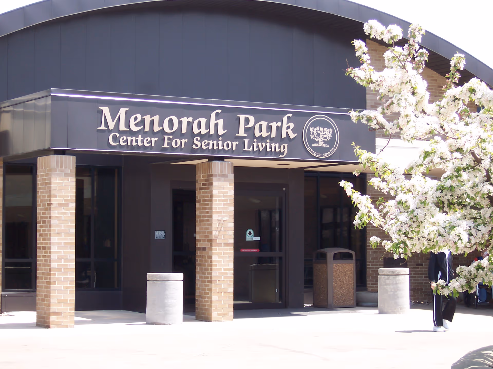 The Menorah Park Center for Senior Living entrance with brick columns and blooming tree.