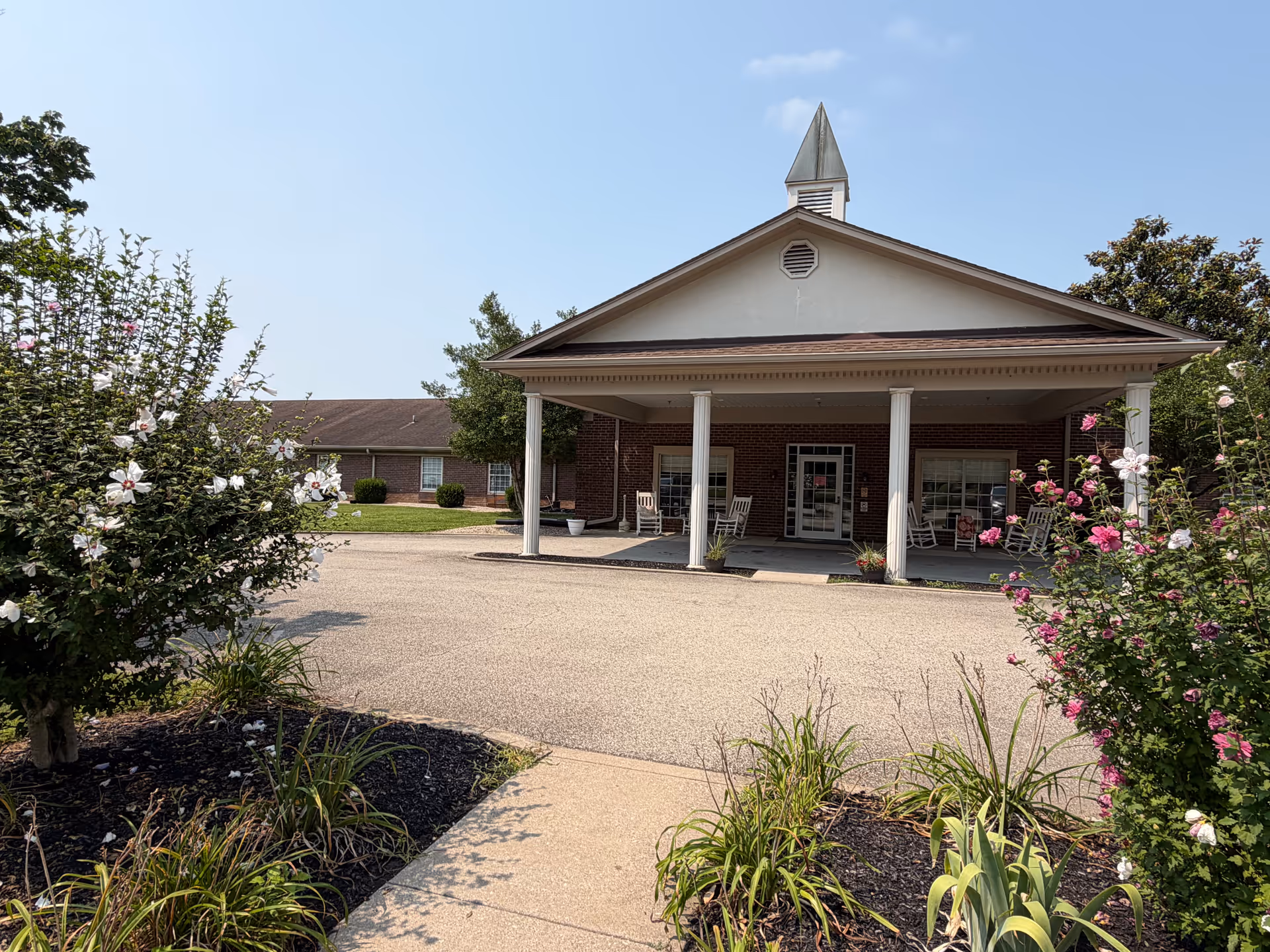 Front view of Green Meadows Health Care Center with covered entrance and rocking chairs on porch.