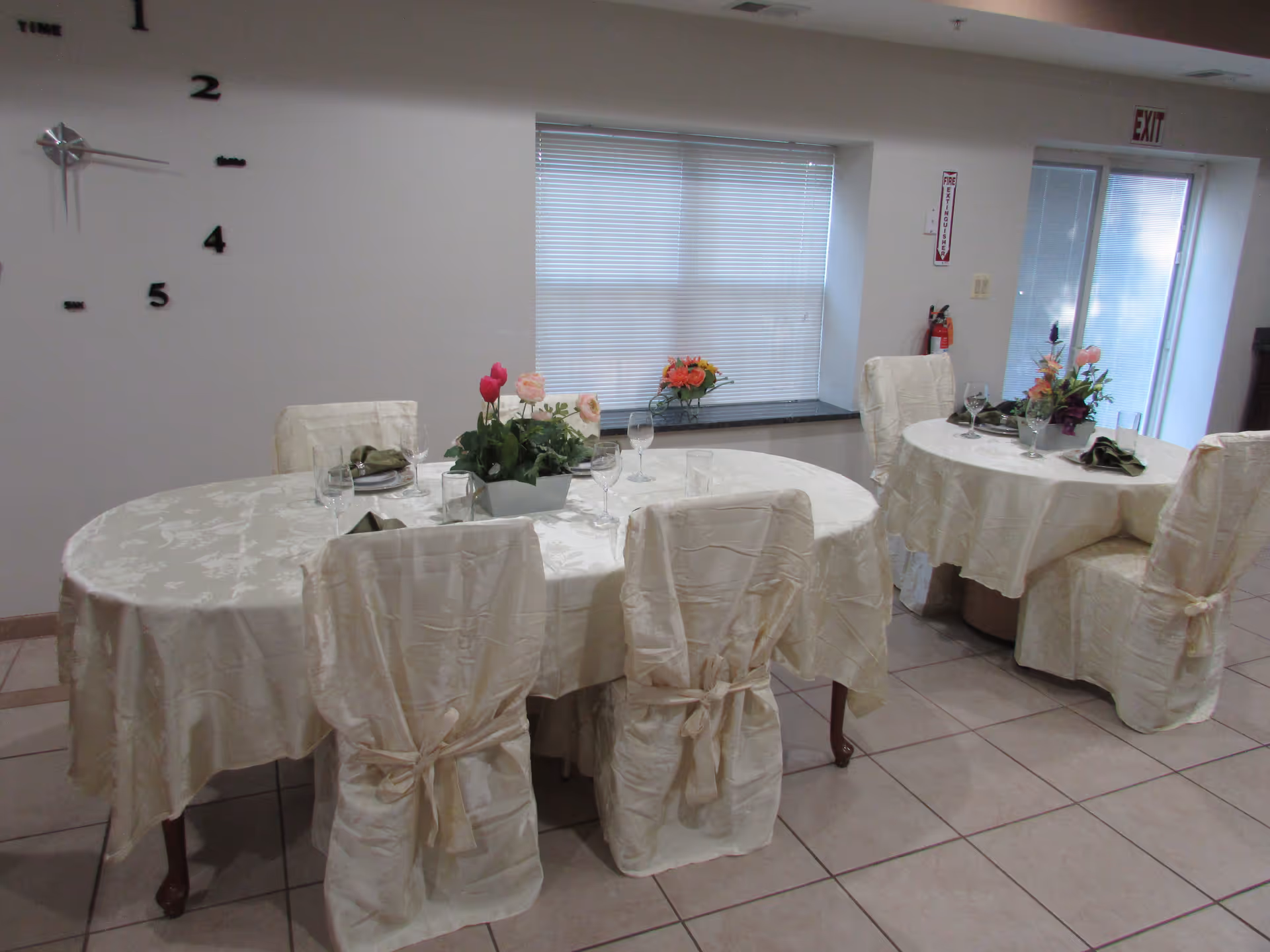 Two round dining tables with white tablecloths, chair covers, and floral centerpieces.