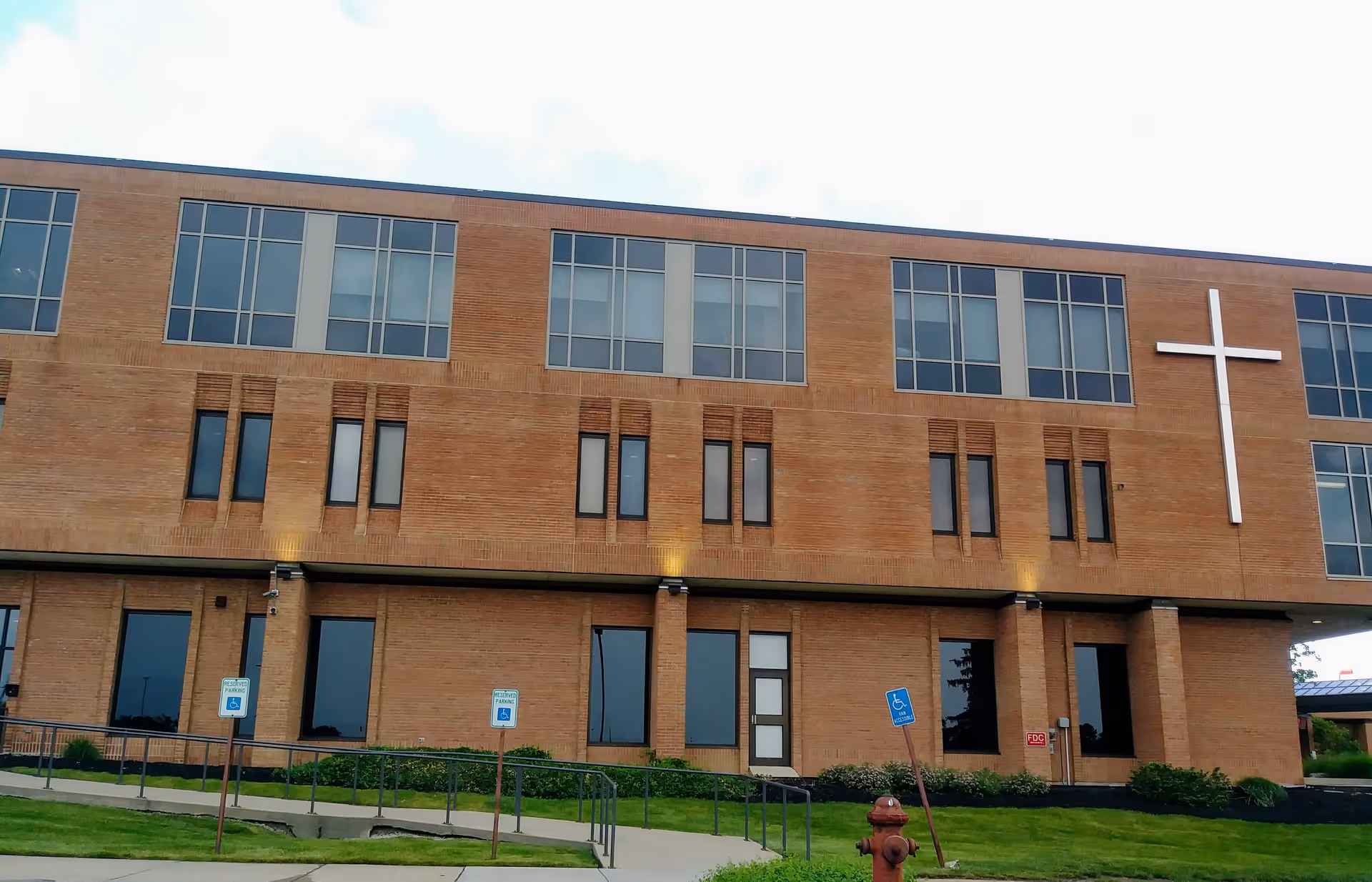The brick hospital building facade features a large white cross and an entrance.